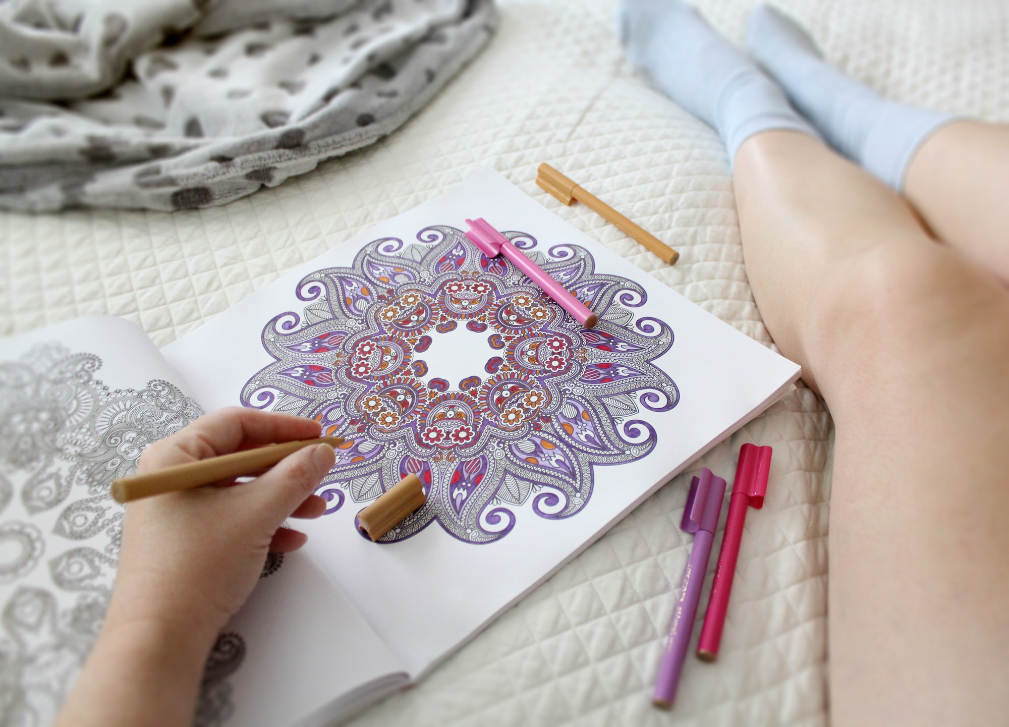 Woman's legs, relaxing in bed on the weekend with pens and a coloring book